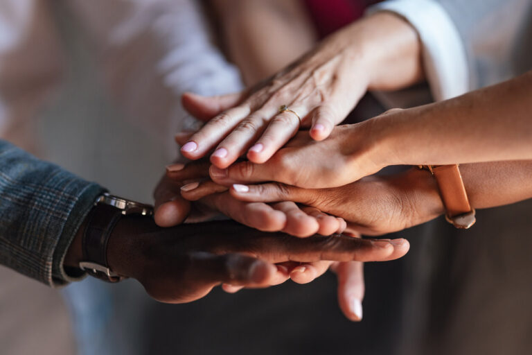 A close-up image of diverse hands stacked together, symbolizing teamwork, unity, and collaboration.